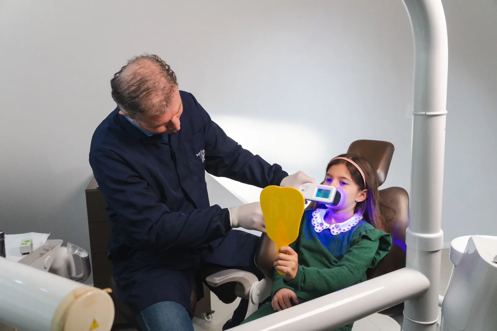 Dentista usando QScan Plus com paciente — luz QLF azul em consulta clínica
